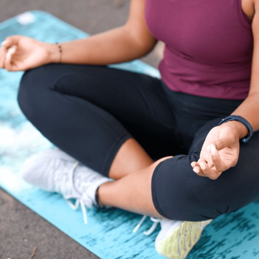 A woman sits cross-legged on the ground as she meditates.