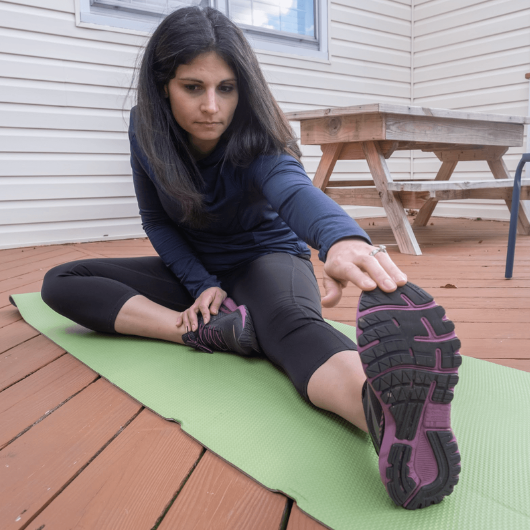 A brunette woman sits on the ground and stretches her legs.
