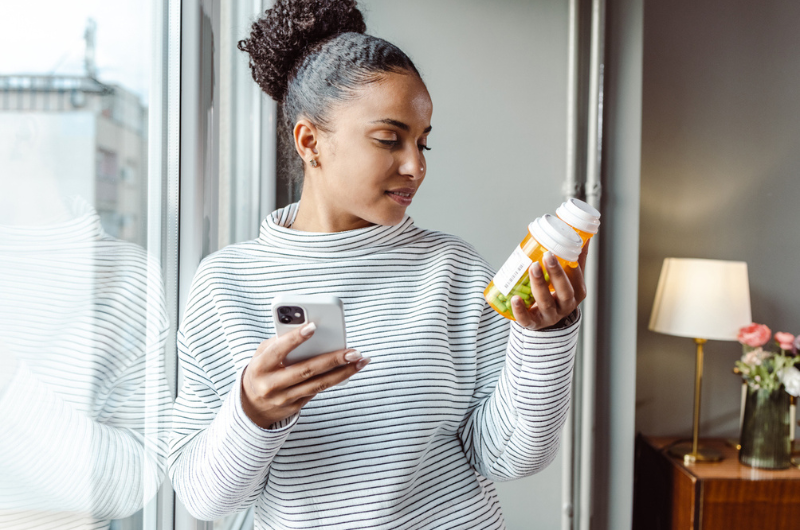 A young woman sits on the sofa researching medicines on her smartphone.