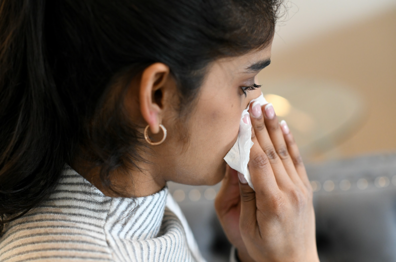 Young woman blows her nose into a tissue.