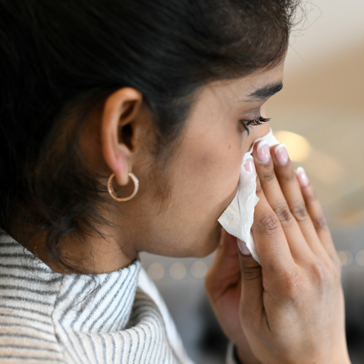 Young woman blows her nose into a tissue.