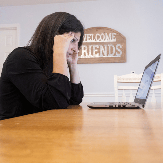 A stressed-out woman holds her hands to her head as she looks at her computer.