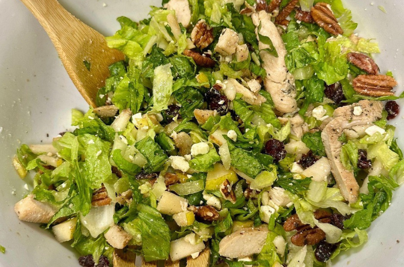 Top-down view of a bowl of autumn chopped chicken salad with mixing spoons.