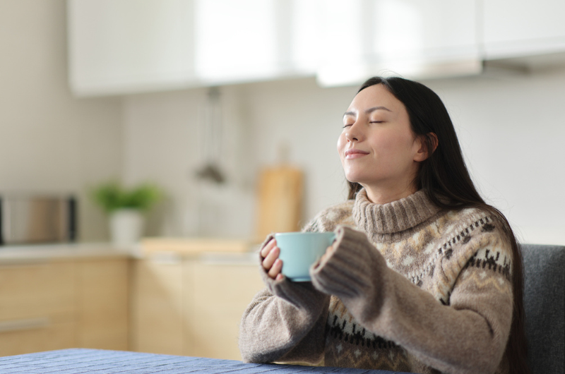Asian woman relaxing and drinking coffee in the kitchen in winter.