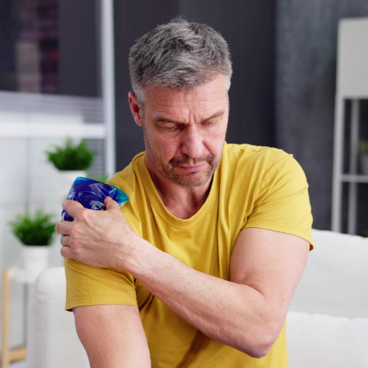 Middle-aged man applies a cool gel pack to his shoulder.