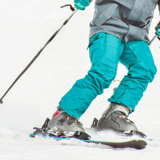 Close up of blue pants and poles of skier going downhill.