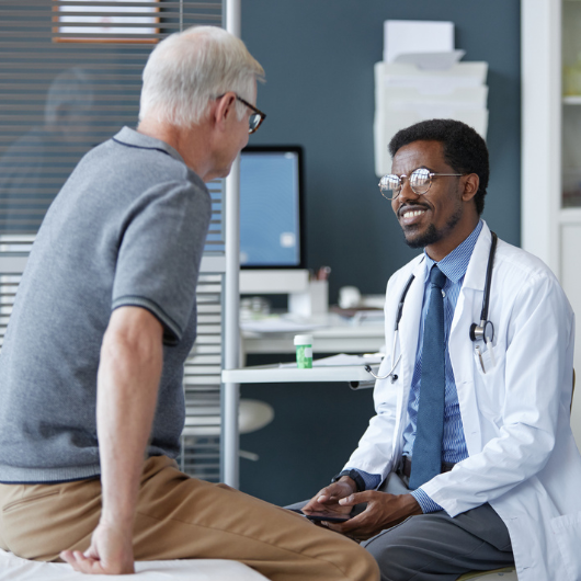 Friendly African American doctor wearing glasses and smiling while listening to senior patient.