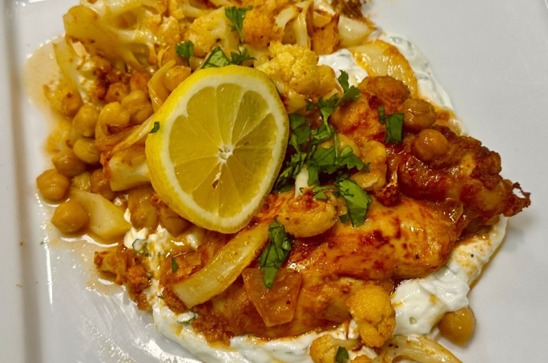 Top-down view of a dish featuring chicken thighs, cauliflower and flavorful herbs and spices.