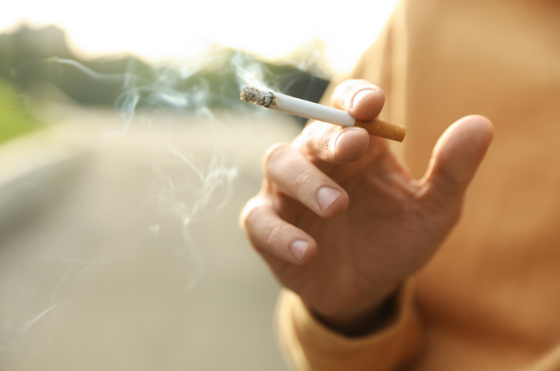 Closeup of a man holding a cigarette outdoors.
