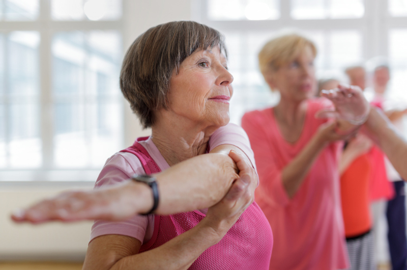 A senior woman stretches her arm in a group class.