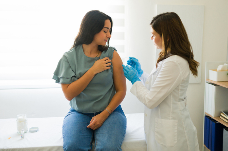 Doctor in gloves is administering allergy shots to a young woman in a medical office.