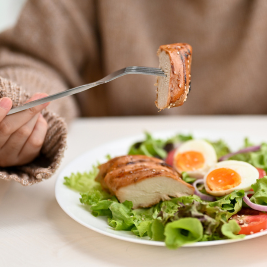 Woman eating a fresh healthy salad with grilled chicken breast.