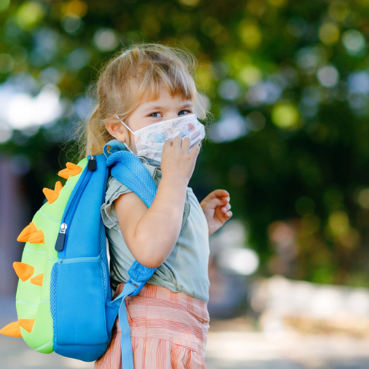 Toddler girl on her way to school while wearing a medical mask.