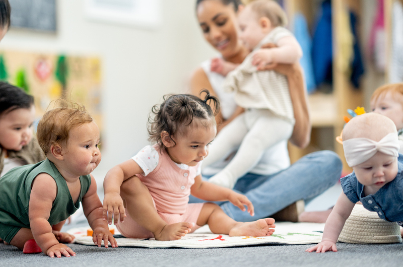 A group of babies play closely together on the floor.