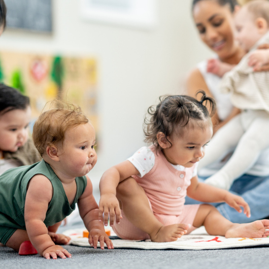 A group of babies play closely together on the floor.