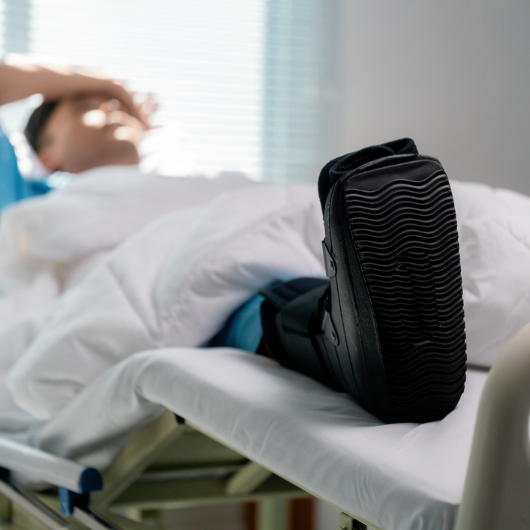 Patient wearing a walking boot lying in a hospital bed while recovering from bunion surgery.