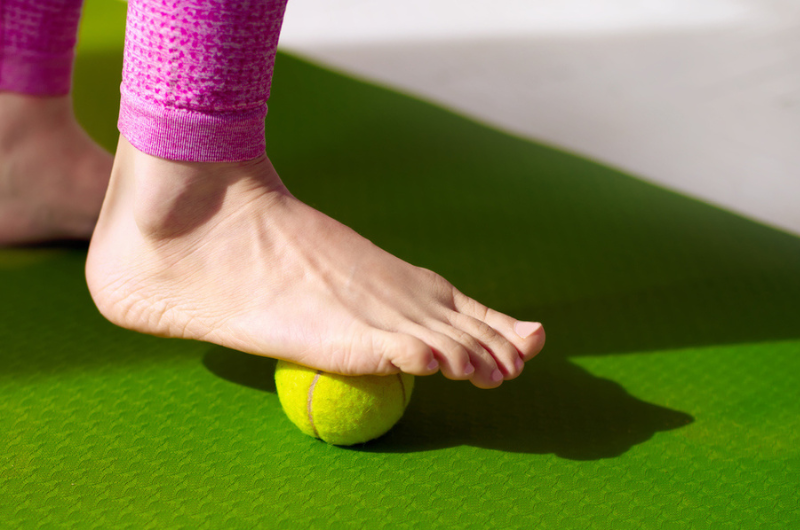 a foot using tennis ball to roll out pain