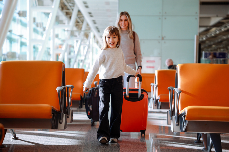 A young mom and daughter walking to board their flight in an airport terminal.