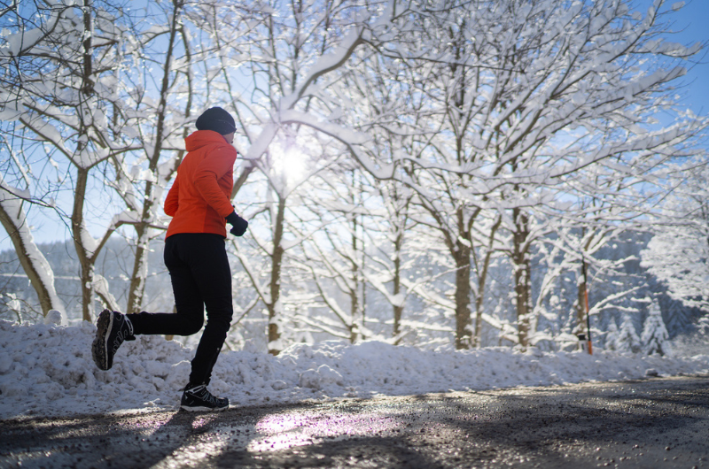Female athlete jogs on a road with slush and snow in background.