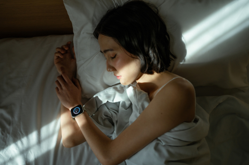 Woman sleeping peacefully in bed, wearing a smart watch to track her sleep patterns.