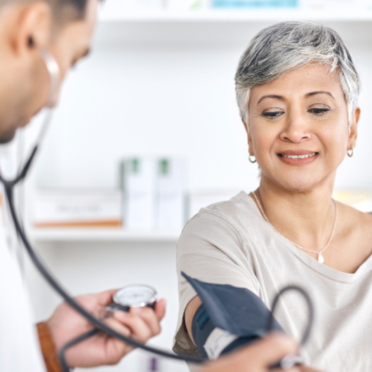 Image shows a doctor checking a woman's blood pressure in a clinical setting.