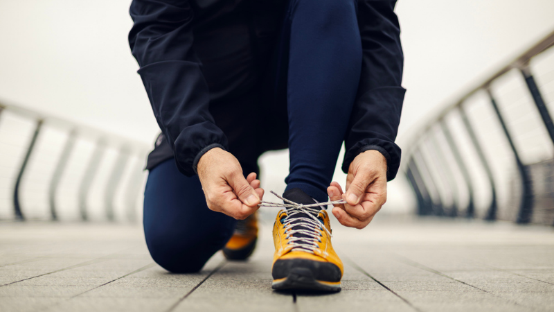 Mid-adult runner bending on an urban bridge path tying a bright yellow running shoe.