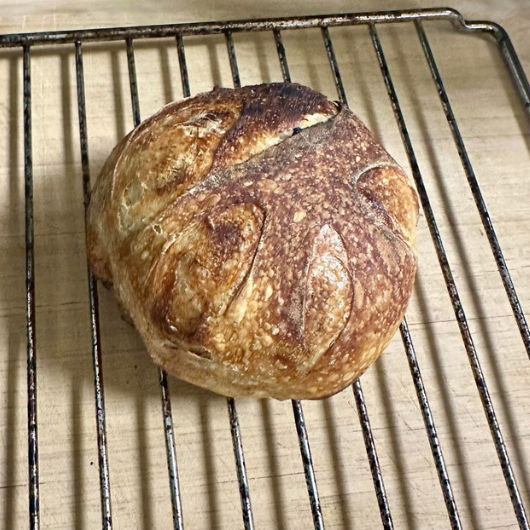 After baking, a sourdough loaf sits on a cooling rack.