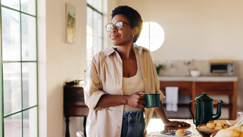 Thoughtful Brazilian woman looking away while holding a cup of coffee in her kitchen.