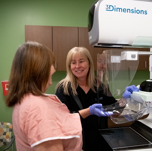 Nurse standing with patient in front of a mammogram machine.