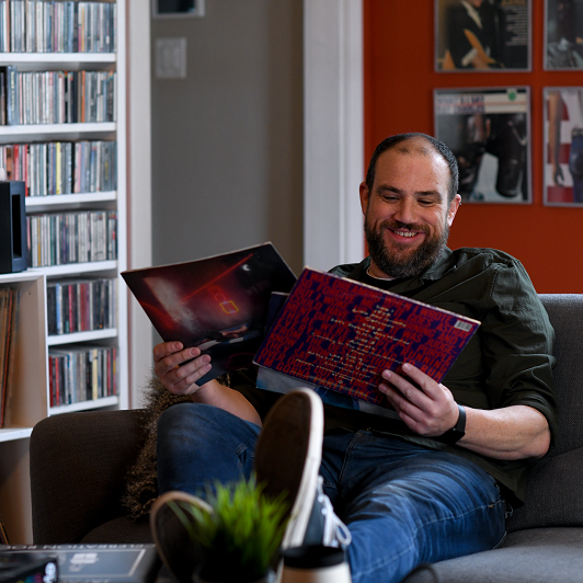 Matt Kleinschmidt, a young man, sitting on a couch holding vinyl records while smiling