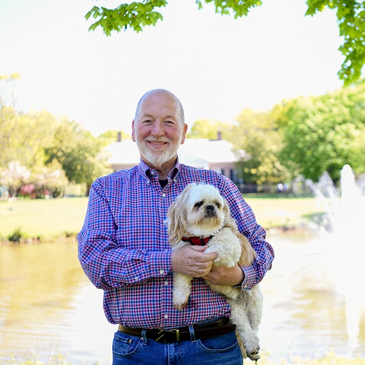 Patient Dan Reiss, holding his dog, Jake, smiling outside.