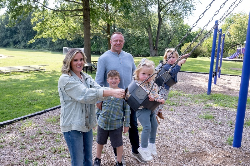 Trista Harper and her family smiling, enjoying the park. Riding bikes, pushing the stroller, and swinging on the swings.