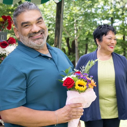 Carlos Mercado holding a bouquet of flowers smiling.