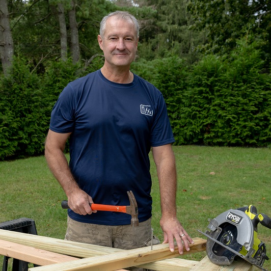 John Sherrod smiling and wood working outside.