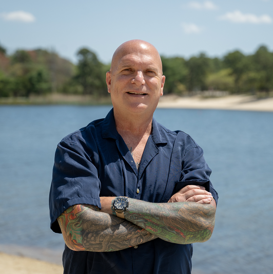 Leonard DiMatteo standing, smiling with his arms crossed, in front of a body of water.