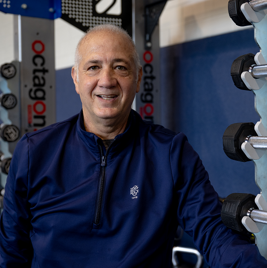 Anthony Lucia smiling at the gym, standing in front of some weights.
