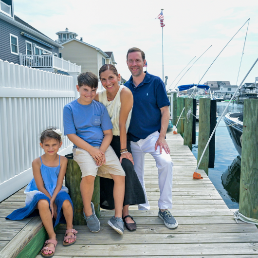 45-year-old Eva Maravelias sits on a dock next to a boathouse with her son, daughter and husband.