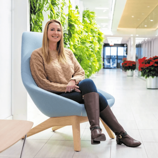 Nicole Mooney, a young mother of three, sits in a hospital lobby and smiles at the camera.
