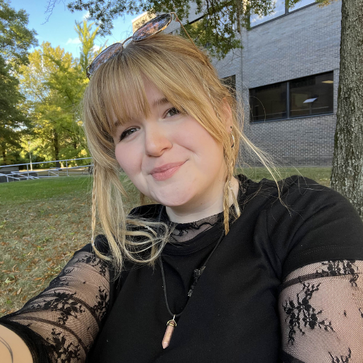 College student sits by a tree.