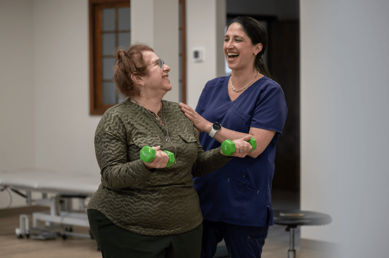 Mary Ann Brancato holds dumbbells and smiles at her therapist.