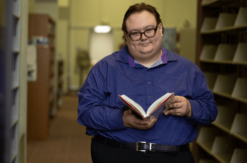 36-year-old Gary Galgoci holds an open book and smiles at the camera.
