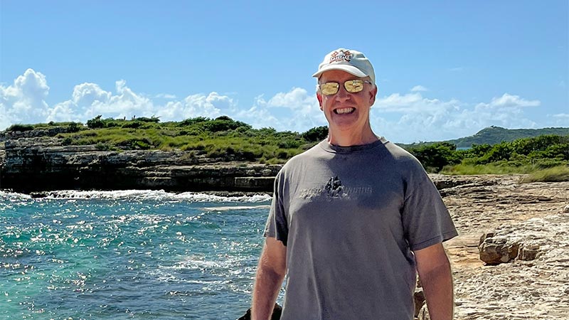 Eric Lewanda smiles in front of a turquoise ocean background.