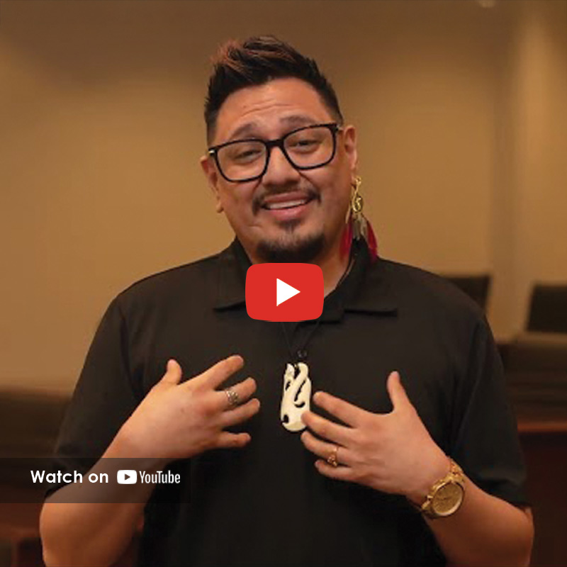 Man speaking in a church setting, wearing glasses and a pendant, sharing a personal story