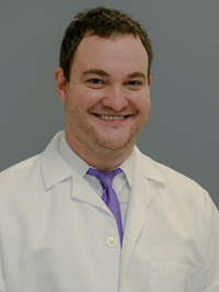 Man with short brown hair smiling while wearing a white lab coat