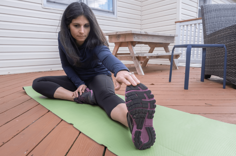 A brunette woman sits on the ground and stretches her legs.