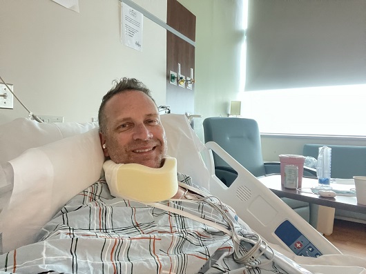 Gerald Branim in the hospital recovering after phrenic nerve reconstruction. There is a bandage around his neck and he is smiling.