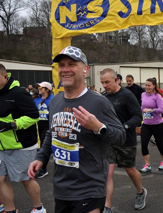 Gerald smiling and waving as he is running in a race.